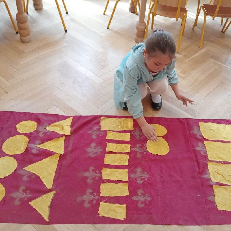 dzieci ozdabiaja królewski dywan figurami geometrycznymi